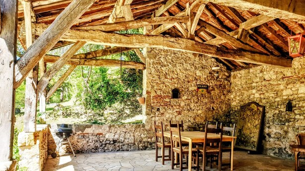 Un espace de restauration extérieur de style rustique, avec des murs en pierre et des poutres en bois, comprenant une table et des chaises en pierre.