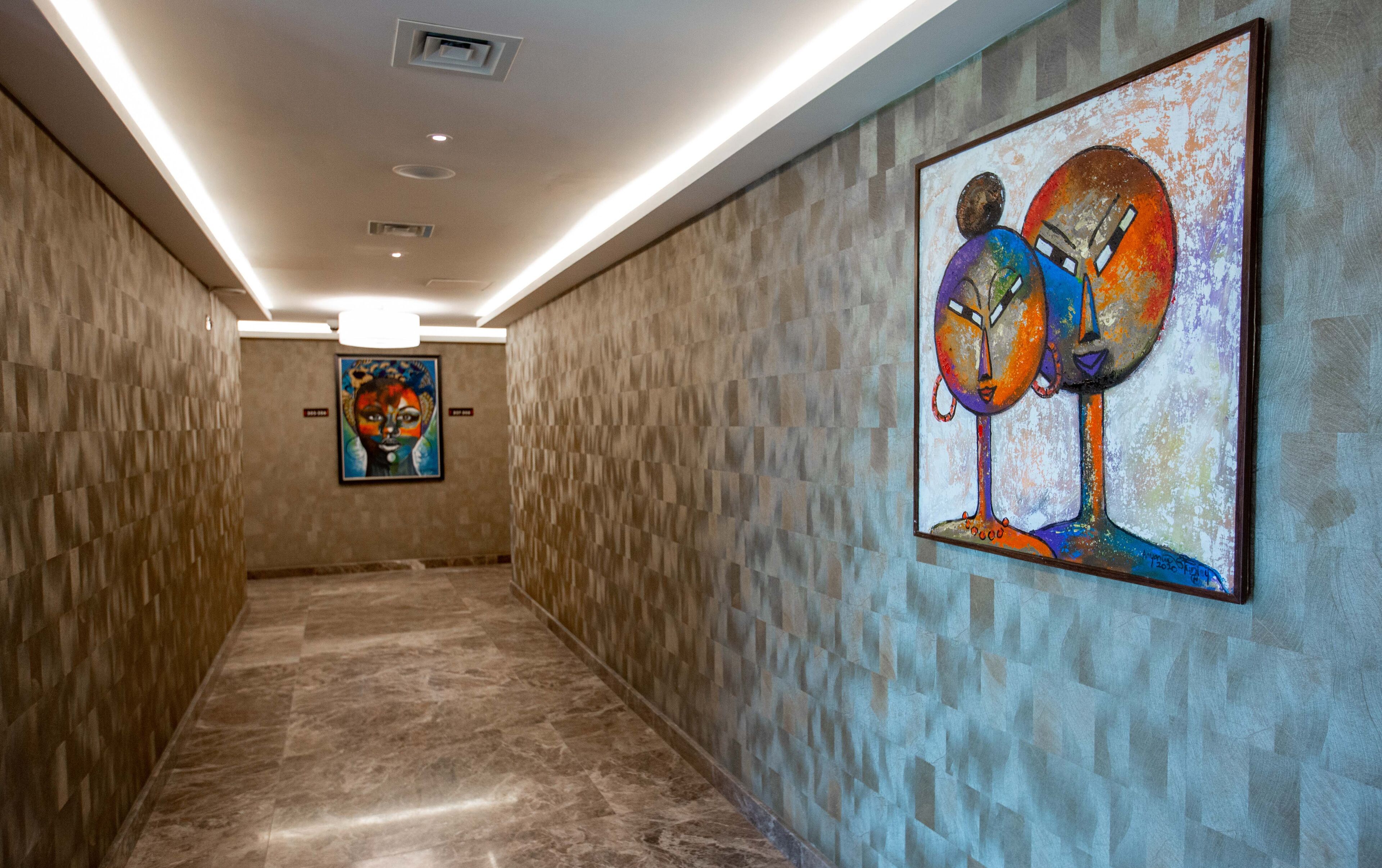 Um corredor com piso de mármore, paredes texturizadas e duas obras de arte.