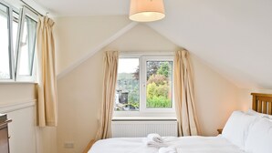 Une chambre à coucher avec un grand lit, une fenêtre avec des rideaux, un radiateur et une tête de lit en bois.