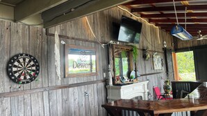 A rustic bar area with a dartboard, a mirror, and a television mounted on the wall.