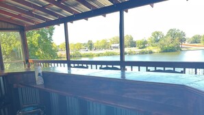 A bar area with a view of a lake, wooden deck, and outdoor seating.