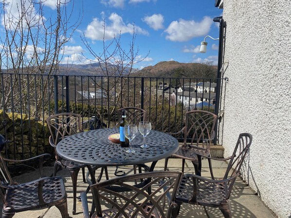 A round metal table with chairs, a bottle, and two glasses on a balcony with a view of houses and mountains. - 3 bedroom accommodation in Ambleside (Ambleside)