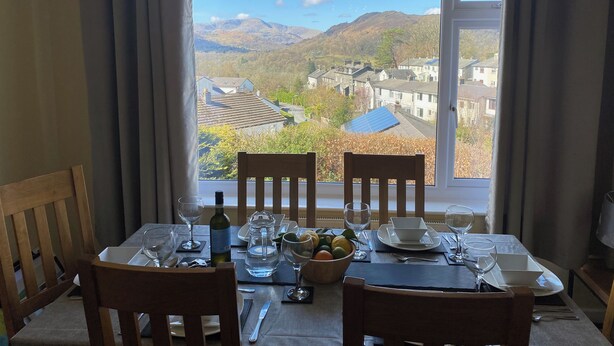 Une table à manger dressée pour deux personnes, avec vue sur un paysage montagneux par une grande fenêtre.