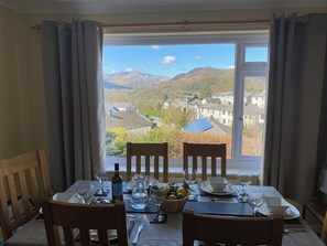 A dining table set for two with a view of a mountainous landscape through a large window. - 3 bedroom accommodation in Ambleside (Ambleside)