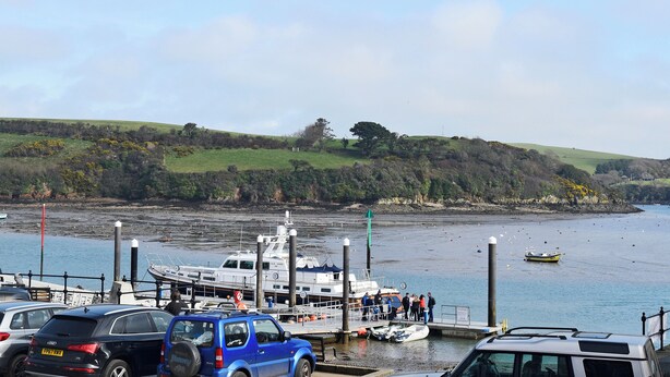 A marina with boats docked, a hilly landscape in the background, and a clear sky.