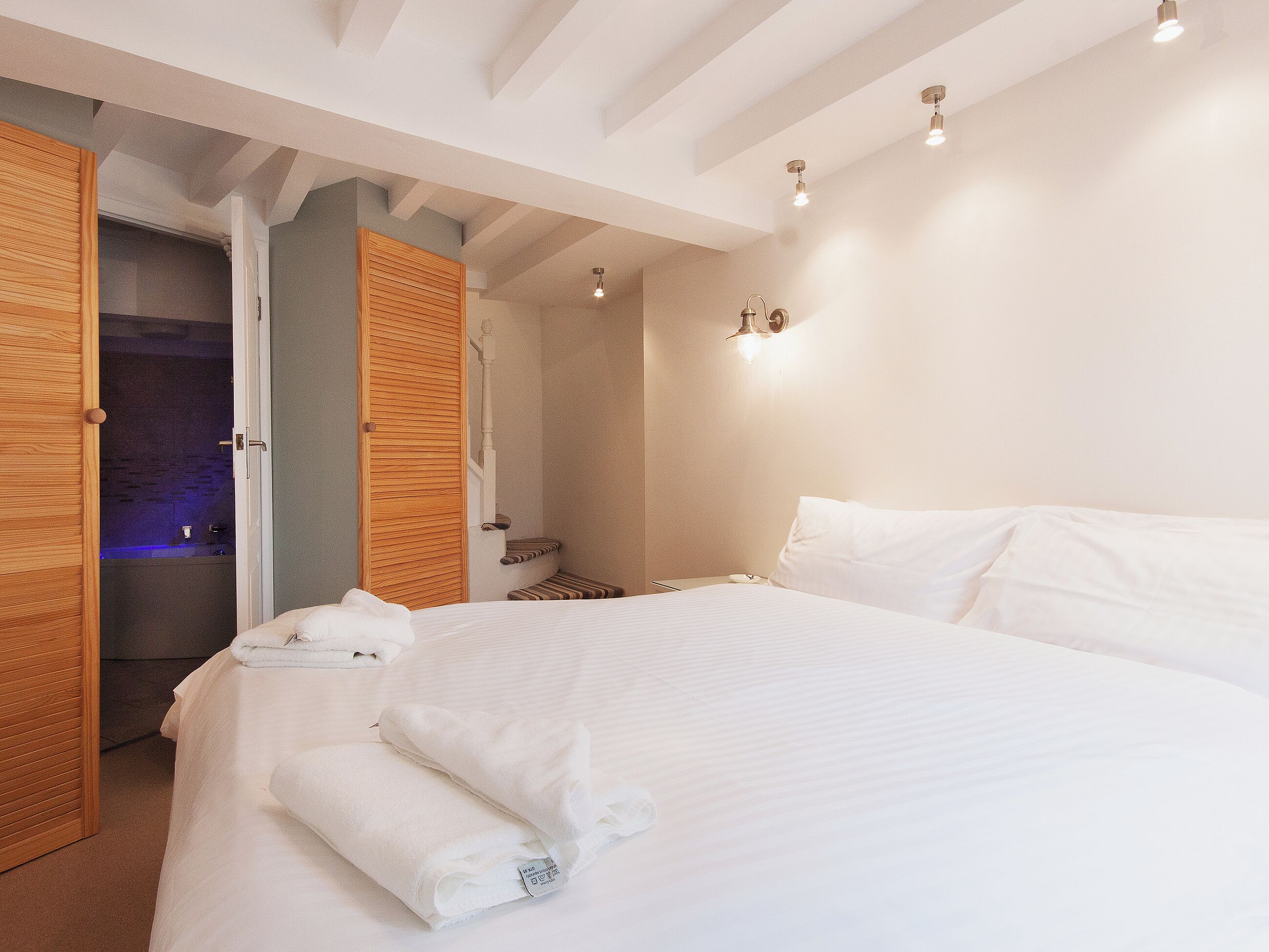 A bedroom with a large bed, wooden doors, and a bathroom visible through an open door.