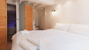 A bedroom with a large bed, wooden doors, and a bathroom visible through an open door.