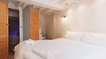 A bedroom with a large bed, wooden doors, and a bathroom visible through an open door.