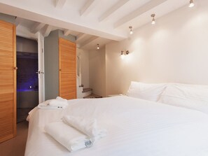 A bedroom with a large bed, wooden doors, and a bathroom visible through an open door.