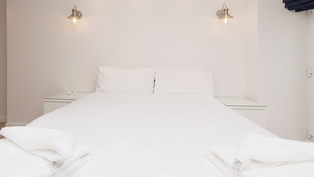 A clean, minimalist hotel room with a neatly made bed, bedside tables, and wall-mounted lighting. - 1 bedroom accommodation in Fore St (Fore St)