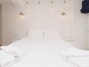 Habitación de hotel limpia y minimalista con cama bien hecha, mesitas de noche e iluminación empotrada en la pared.