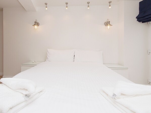 A clean, minimalist hotel room with a neatly made bed, bedside tables, and wall-mounted lighting.