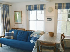 A room with a blue sofa, a dining table with a bird-patterned tablecloth, and a window with a blue and white valance.