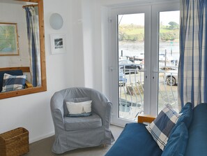 Una habitación con un sillón gris, un sofá azul, piso de madera, un mapa en la pared y vista a un muelle con barcos y coches.