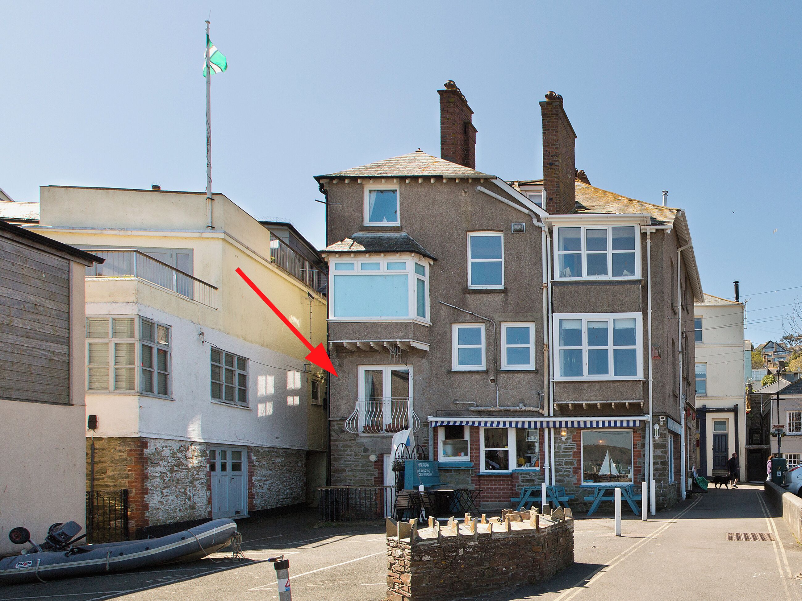 A multi-story building with a visible ground-floor shop, a flag on a pole, and a boat tied to the building.