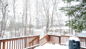 A wooden deck with snow-covered railings, a small shed, and a snow-covered tree in the background.