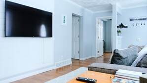 A living room with a flat-screen TV mounted on the wall, a wooden coffee table with a remote control, and a grey sofa.