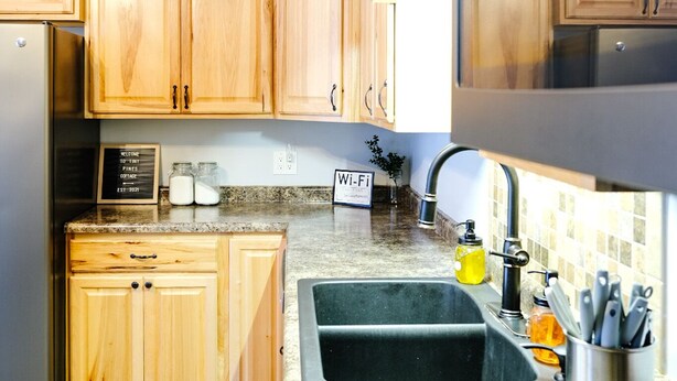A kitchen with wooden cabinets, a granite countertop, a stainless steel sink, and a Wi-Fi sign.