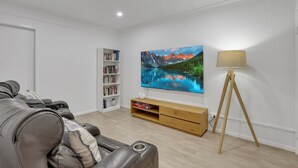 Uma sala de estar moderna com um sofá de couro, uma estante, uma TV fixada na parede e um abajur.