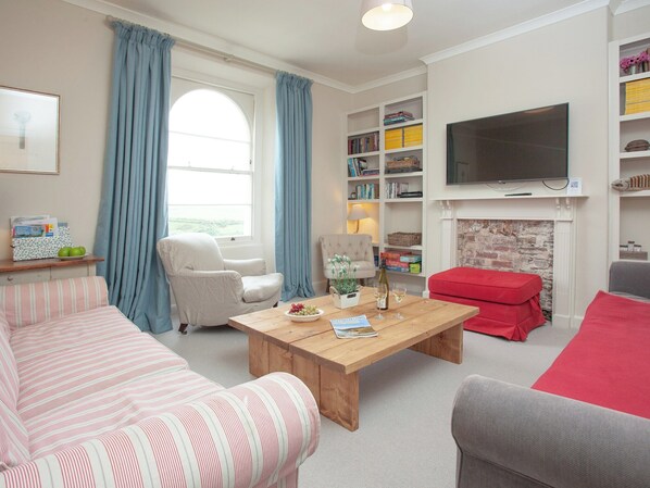 A living room with a sofa, armchair, coffee table, bookshelf, television, and fireplace. - 4 bedroom accommodation in Devon Road (Devon Road)