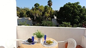 Ein Balkon mit Tisch für zwei Personen, umgeben von weißen Stühlen, mit Blick auf eine Stadtlandschaft und Grünflächen im Hintergrund.