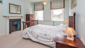 A bedroom with a bed, a dresser, a mirror, a fireplace, and two windows with striped curtains. - 1 bedroom accommodation in Mount Boone (Mount Boone)