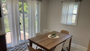 Zona de dinar amb taula de fusta, cadires blanques i un petit arranjament floral al centre.