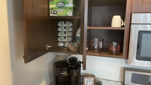 Una cuina amb una cafetera Keurig, un suport per a càpsules de cafè, una tassa i una petita planta.