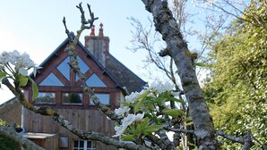 Ein Haus mit einem geneigten Dach und Schornstein, umgeben von einem gepflegten Rasen und einem Baum mit weißen Blüten.
