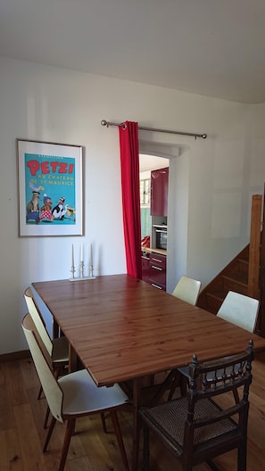 A dining area with a wooden table and chairs, a framed picture on the wall, and a red curtain.