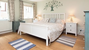 A bedroom with a bed, two bedside tables, a dresser, a window with curtains, a wall-mounted tree decoration, and a lamp on each bedside table. - This apartment is just a short walk from the centre of Salcombe. (Salcombe)
