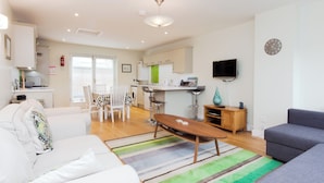 A modern living room with a sofa, a coffee table, and a grey couch. There is a dining area with a table and chairs, and a kitchen in the background. - This apartment is just a short walk from the centre of Salcombe. (Salcombe)