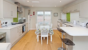 A modern kitchen with white cabinets, a dining table with chairs, a microwave, a stove, and a washing machine. - This apartment is just a short walk from the centre of Salcombe. (Salcombe)