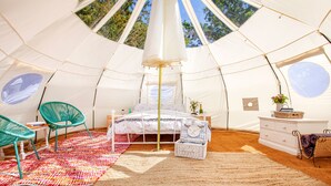 A tent with a bed, chairs, a dresser, and a window.