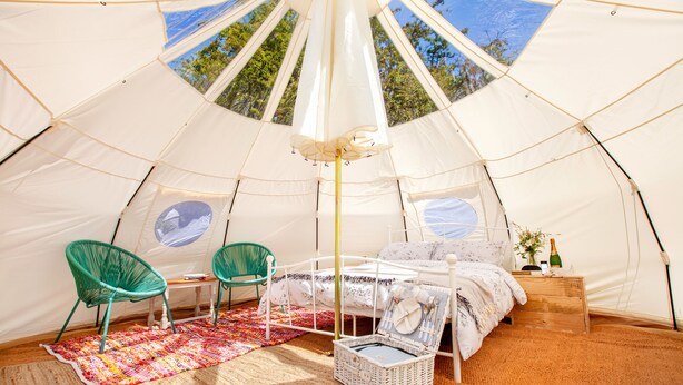 A spacious tent with a bed, two chairs, a small table, and a basket.
