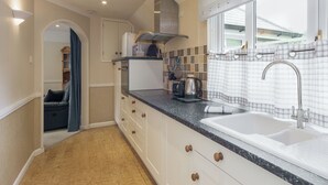 A compact kitchen with a sink, stove, and microwave. There is a window with a curtain and a door leading to another room.