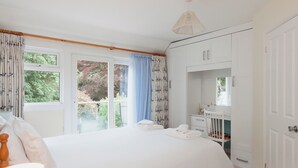 A bedroom with a large bed, a bedside table, a dresser, a mirror, and a window with curtains.