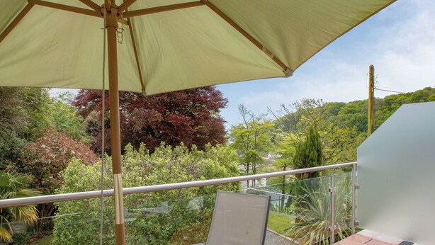 A balcony with a table and chair, a retractable awning, and a view of a garden and hills.