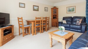 A living room with a TV, wooden dining table, chairs, a blue leather sofa, and a cabinet.