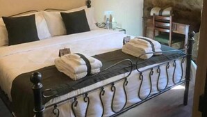 A neatly made bed with pillows and towels, a bedside table with a lamp, and a stone wall in the background. - La  Posada de Leza (Leza)