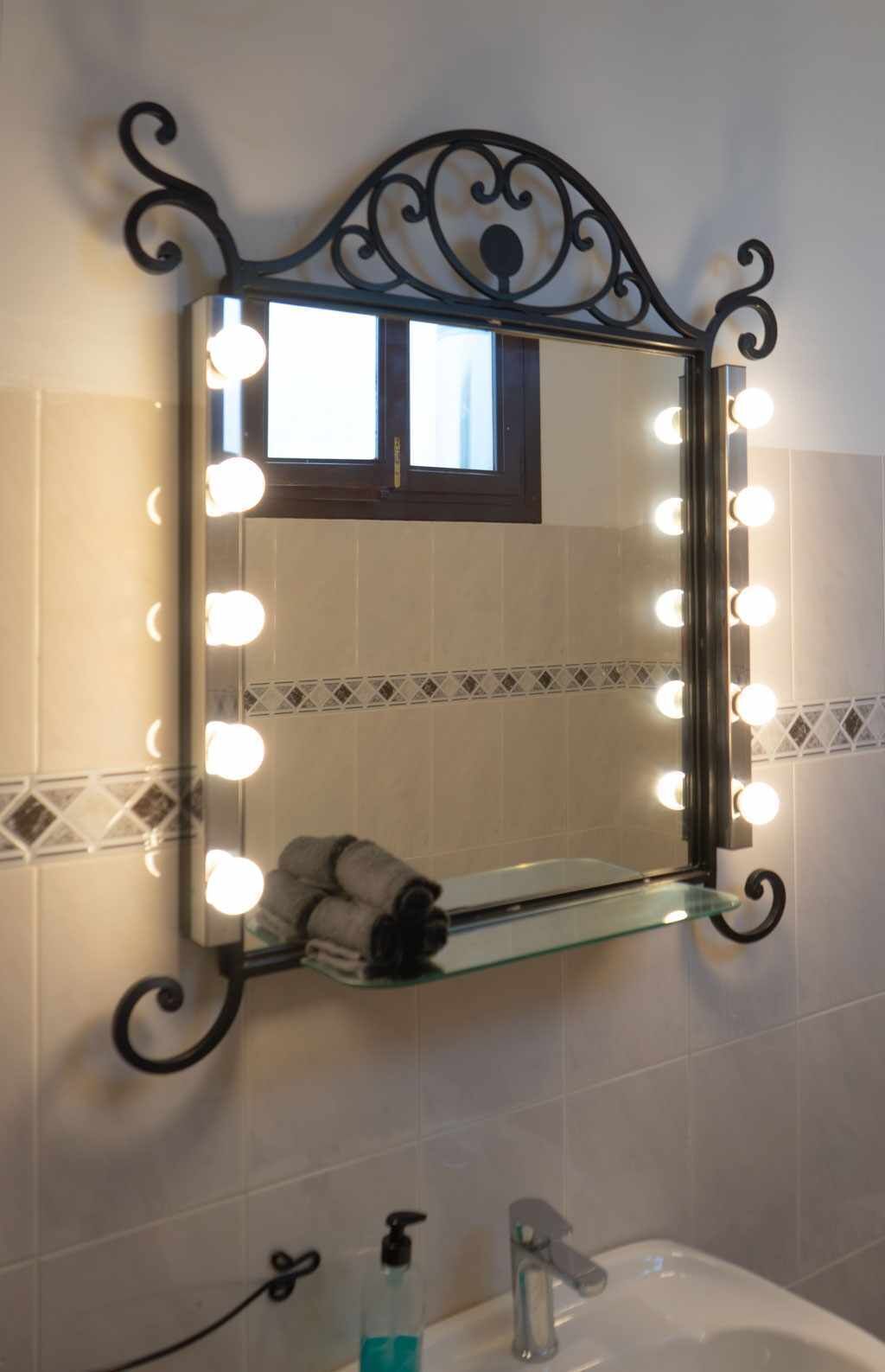 Ein Badezimmer mit Waschtisch, einem beleuchteten Spiegel, einem Handtuchhalter und einem Waschbecken.