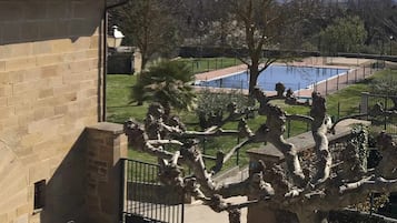 A view from a balcony overlooking a swimming pool, with a stone building and patio furniture visible.