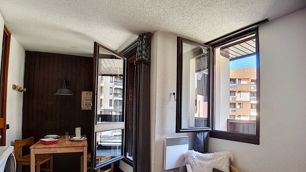 A small, cozy room with a wooden dining table, a chair, and a window with a view of buildings. - travelski home classic - Résidence Origanes - Studio 2 personnes (Les Menuires)