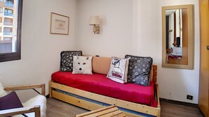 A small, cozy room with a single bed, a chair, a wall-mounted lamp, and a mirror. - travelski home classic - Résidence Origanes - Studio 2 personnes (Les Menuires)