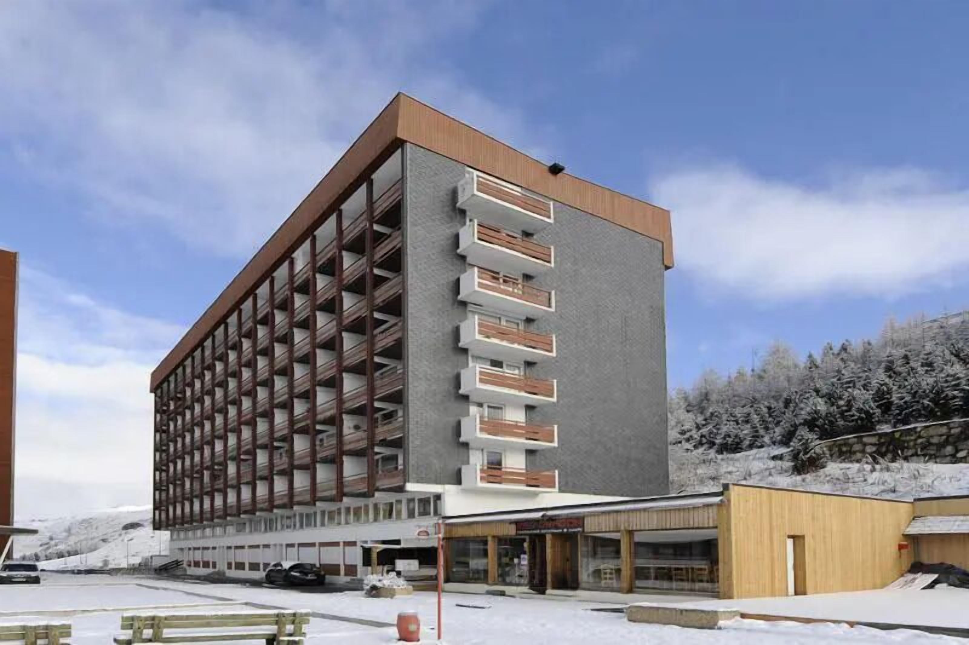 A multi-story hotel with a modern design, featuring a central courtyard and a parking area.