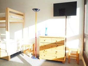 Une chambre avec un lit superposé, un bureau, une commode, une lampe et un téléviseur.