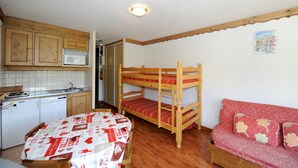 Ein kleines Zimmer mit Etagenbett, einem Esstisch mit roter und weißer Tischdecke, einer Küchenzeile mit Mikrowelle und einer kleinen Couch.