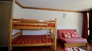 Ein Etagenbett mit einer Leiter, ein rotes Sofa mit gemusterten Kissen und eine Holzzieldecke mit einer Leuchte.