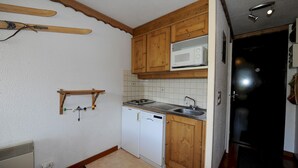 Eine kompakte Küche mit Holzausstattung, einer Mikrowelle, einem Geschirrspüler und einem Ski-Ablagefach.
