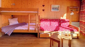 A wooden room with bunk beds, a sofa, a table, and a lamp. - travelski home classic - Résidence Grande Masse - Studio 3 personnes 709 (Les Menuires)